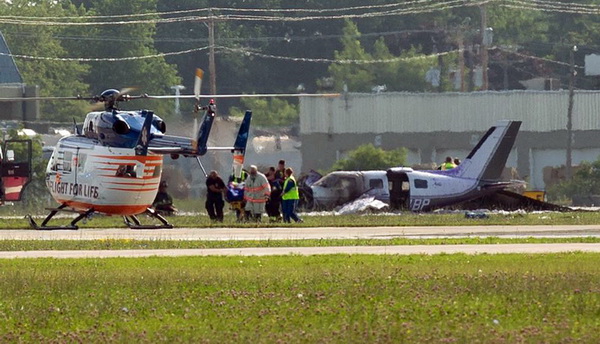 This photo provided by Jeremy Dwyer-Lindgren shows emergency personnel the scene of a small plane crash Wednesday, July 22, 2015 at the Experimental Aircraft Association convention in Oshkosh, Wis. Officials say five people on board the single-engine Piper Malibu were injured when it crashed while landing at the convention. (Jeremy Dwyer-Lindgren/FlightGlobal via AP) MANDATORY CREDIT